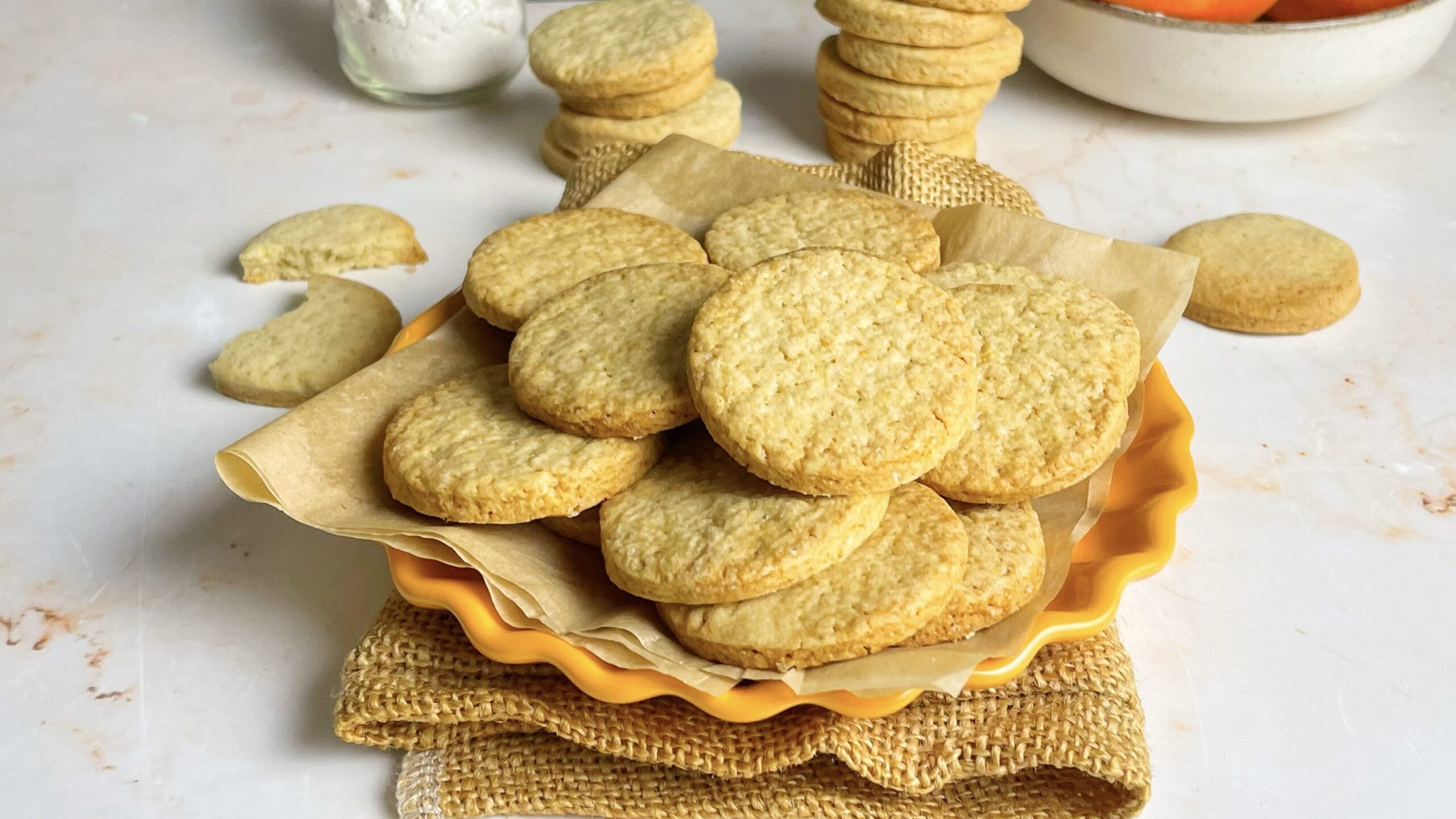 Biscotti di frolla all'arancia su un piatto, con farina e arance sullo sfondo