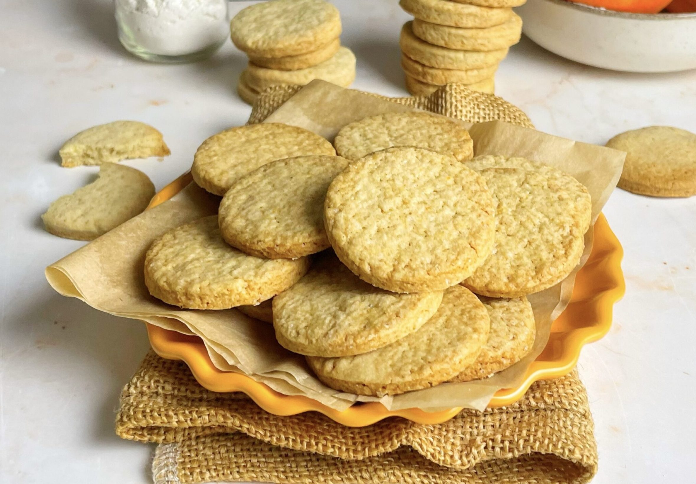 Biscotti di frolla all'arancia su un piatto, con farina e arance sullo sfondo